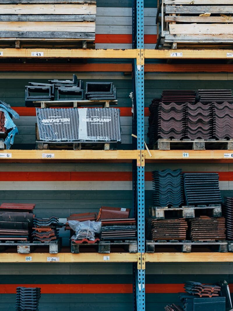 Shelves filled with construction materials like tiles and wood pallets in a warehouse setting.
