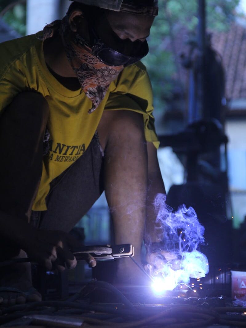 A worker skillfully welding metal in a workshop, wearing protective gear and creating sparks.
